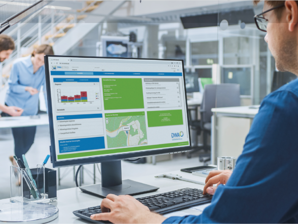 Mann am Schreitisch sitzt am PC auf dem das Online-Portal DWA Betrieb geöffnet ist.