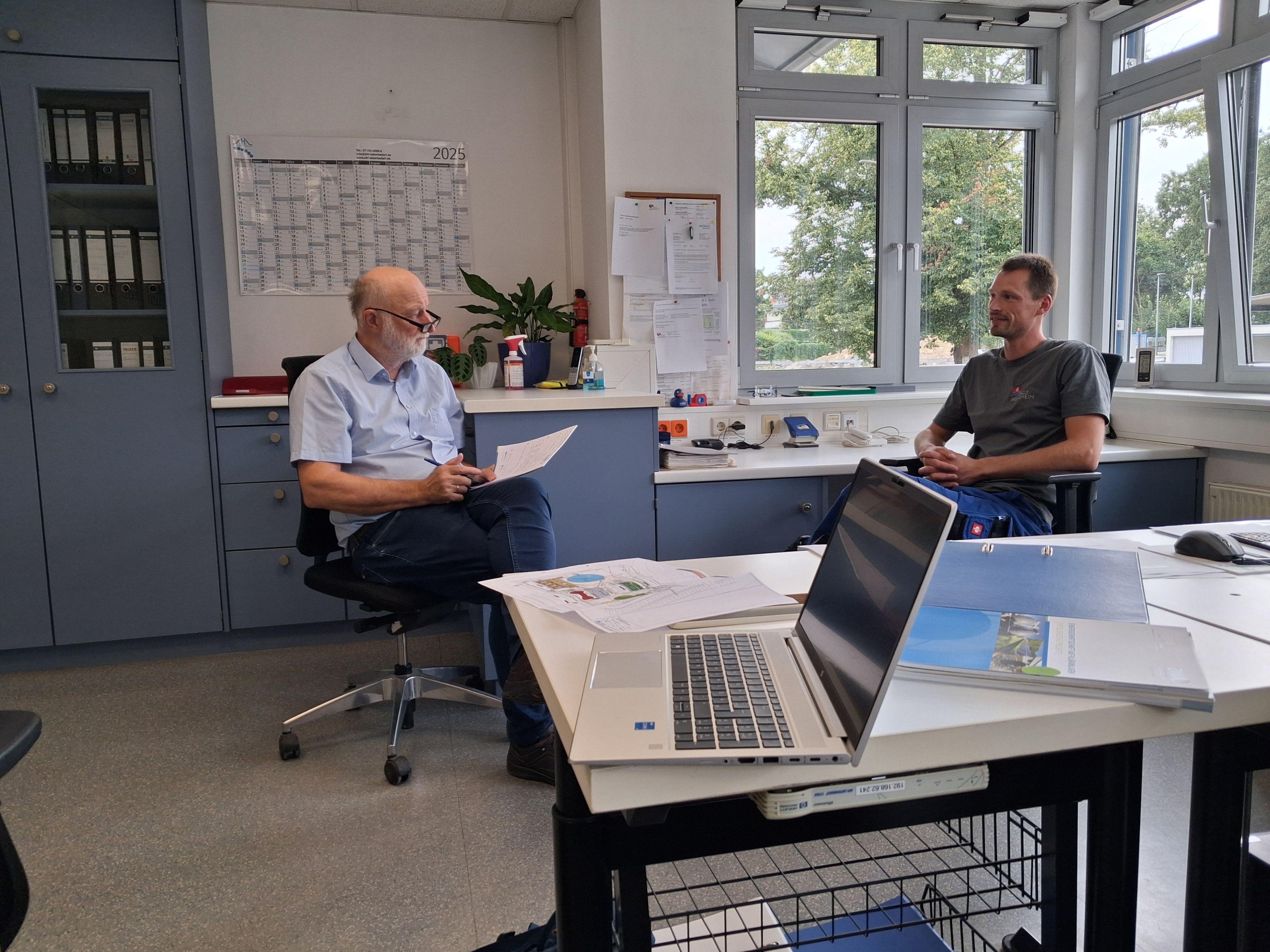 Herr Schwentner und Herr Bezner sitzen in einem Büro auf der Kläranlage Besigheim und besprechen sich bezüglich der Energieeffizienz auf der Kläranlage.